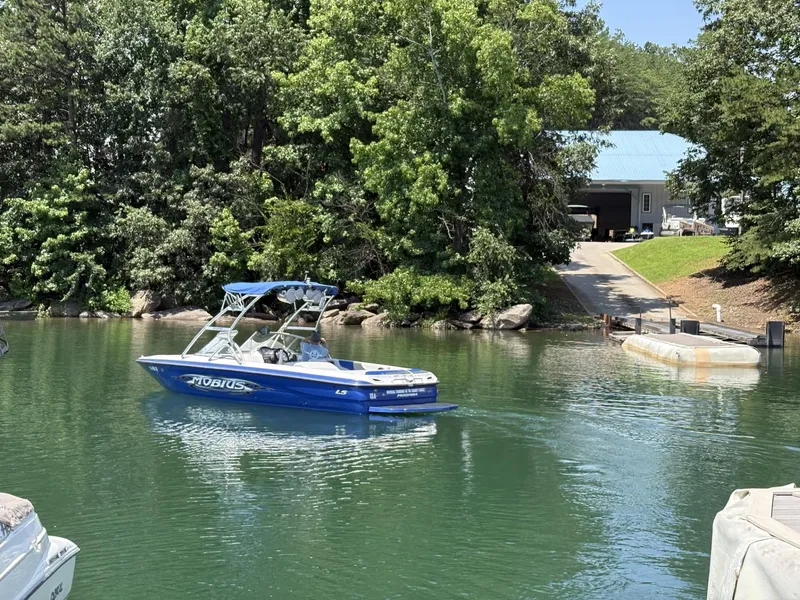 Slide: The Image of 2004 Moomba MOBIUS LS boat on a serene lake near a wooded shoreline. - 10