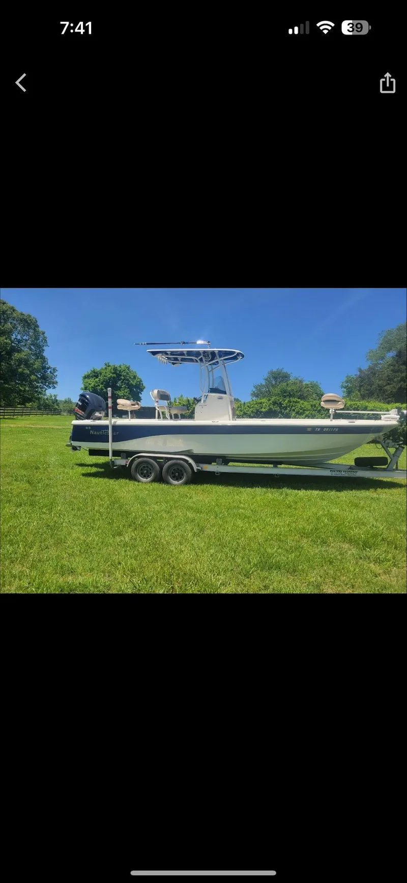 Slide: The Image of 2014 NauticStar 244 XTS boat on trailer, parked on grassy field under clear blue sky. - 1