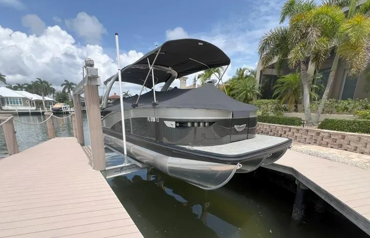 Slide: The Image of 2022 Bennington RX 25 RXFBA pontoon boat docked under a canopy, surrounded by tropical scenery. - 2