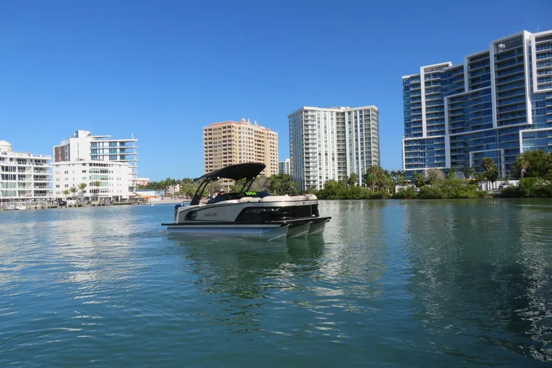 Slide: The Image of 2026 Avalon Excalibur LTD 25’ Tritoon on water, cityscape background, clear blue sky. - 94