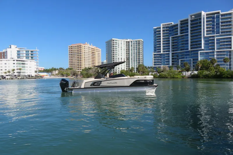 Slide: The Image of 2026 Avalon Excalibur LTD 25’ Tritoon on water, cityscape background, sunny day. - 96