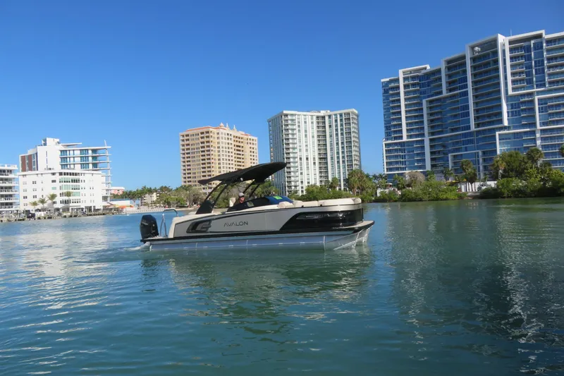 Slide: The Image of 2026 Avalon Excalibur LTD 25’ Tritoon on water, cityscape background, sunny day. - 93