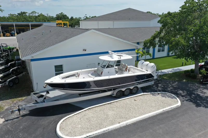 Slide: The Image of 2026 Jupiter 340LS boat on trailer near building, surrounded by trees and equipment. - 37