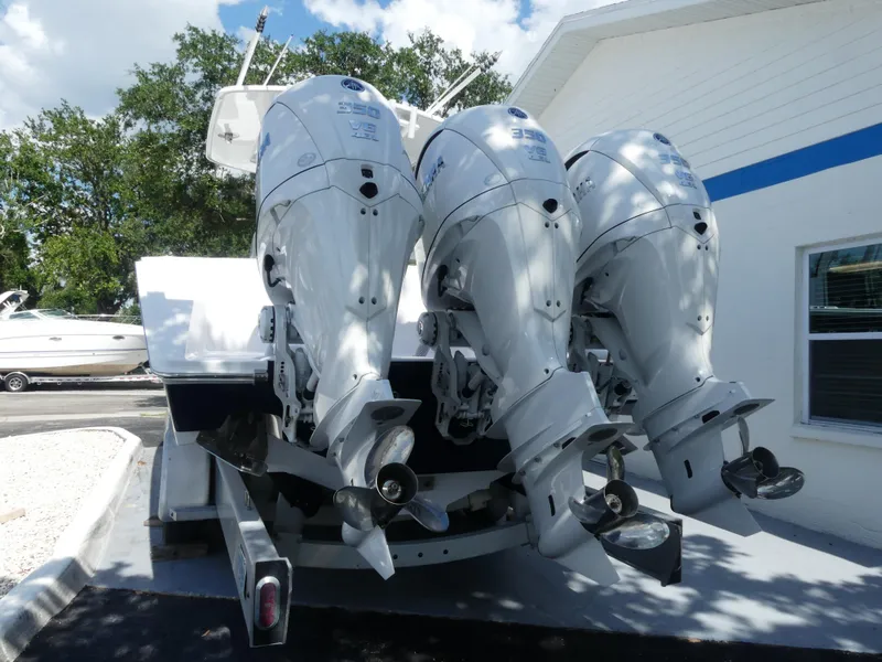 Slide: The Image of Triple outboard motors on a 2026 Jupiter 340LS boat, parked near a white building. - 7