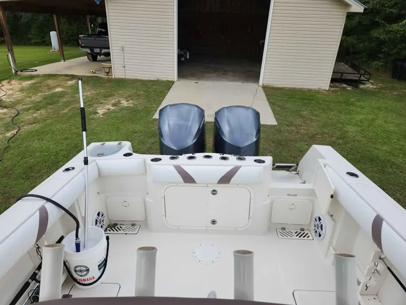 Slide: The Image of 2013 Sailfish 290 CC boat with twin engines, parked near a garage on grassy area. - 11