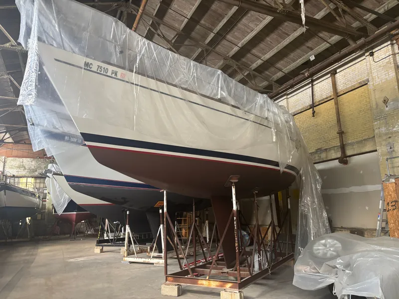 The Image of 1987 Holby Tripp sailboat in a warehouse, covered with plastic sheeting, on a stand. - 0