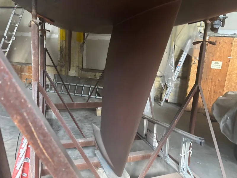 Slide: The Image of 1987 Holby Tripp sailboat keel in a workshop with ladders and supports. - 10