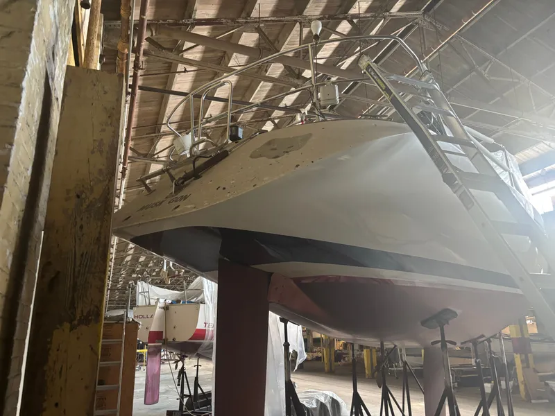 Slide: The Image of 1987 Holby Tripp boat in a warehouse, supported by stands, with a ladder beside it. - 4