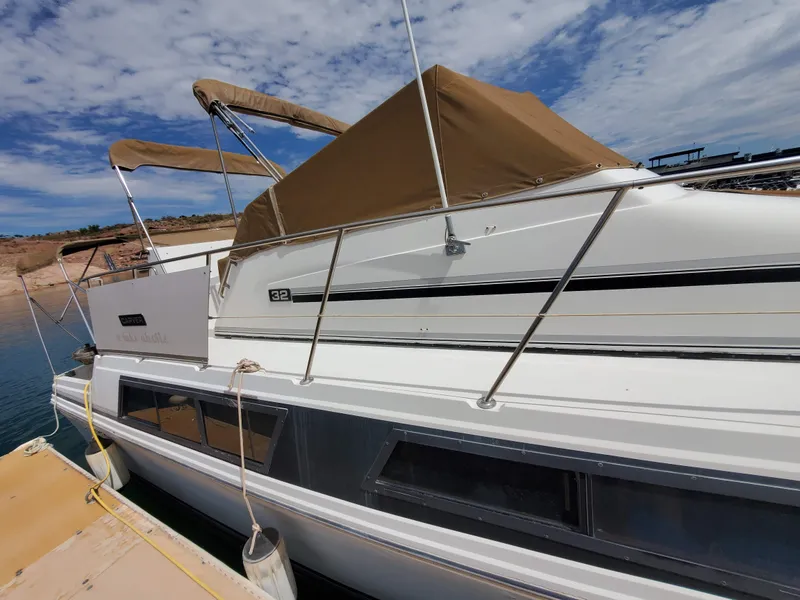 Slide: The Image of 1986 Carver Mariner 32x14.3 boat docked, featuring a beige canopy and sleek white exterior. - 23
