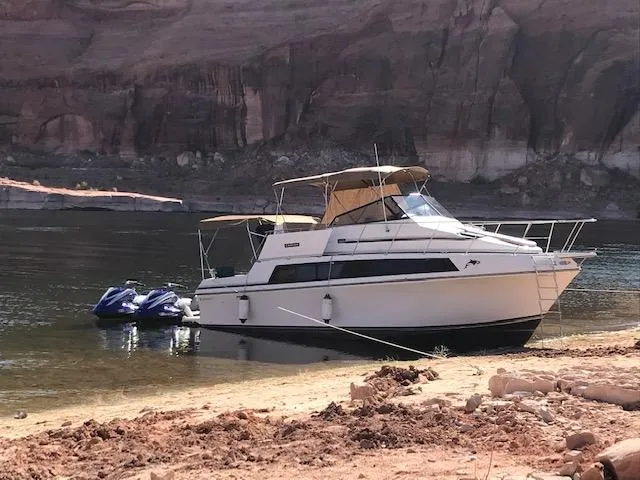 Slide: The Image of 1986 Carver Mariner 32x14.3 boat anchored by rocky shore with jet skis. - 6