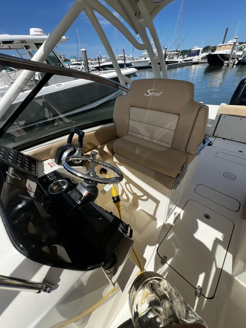 Slide: The Image of 2019 Scout 255 Dorado boat interior with steering wheel and beige seating at marina. - 12