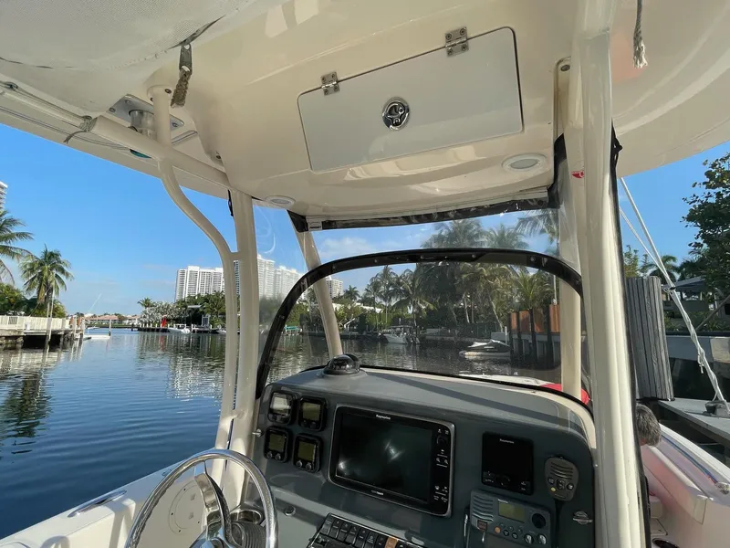 Slide: The Image of 2013 Pursuit C 260 Center Console boat interior with navigation equipment, docked by palm trees. - 15