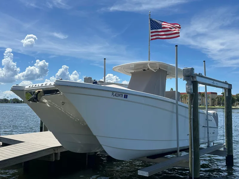 The Image of 2024 World Cat 280ccx boat on lift, American flag, clear sky, waterfront view. - 0