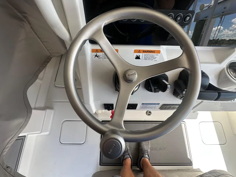 Slide: The Image of 2024 World Cat 280ccx steering wheel and controls, featuring warning labels and footrest. - 33