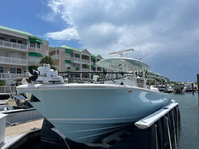 The Image of 2019 Cobia 320 Center Console boat docked at marina with waterfront condos in background. - 1