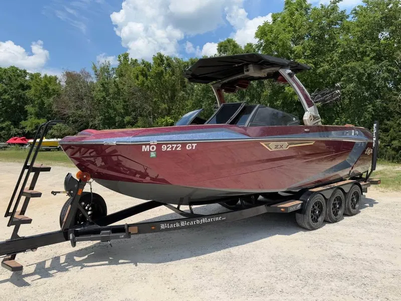Slide: The Image of 2024 Tigé Ultré 25ZX boat on trailer, parked outdoors with trees in background. - 1