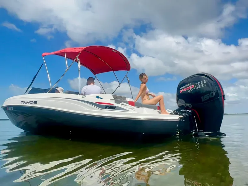 Slide: The Image of 2024 Tahoe T21 boat with red canopy on calm water under blue sky. - 11