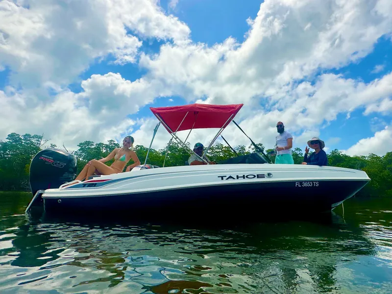 Slide: The Image of 2024 Tahoe T21 boat with passengers, red canopy, on calm water under blue sky. - 12