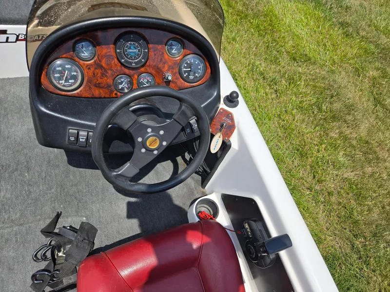 Slide: The Image of 1998 Triton Tr-17 boat dashboard with steering wheel and gauges, red seat, and grassy background. - 14