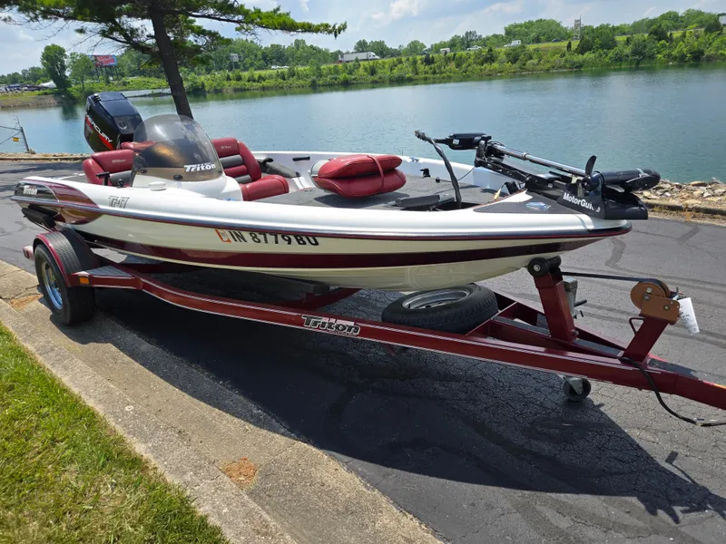 Slide: The Image of 1998 Triton Tr-17 boat on trailer by a lake, featuring red and white design. - 3