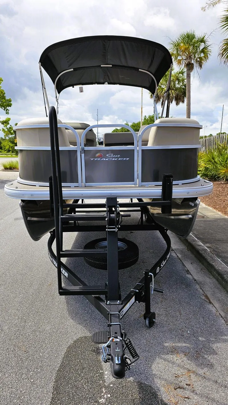 Slide: The Image of 2025 Sun Tracker Party Barge 18 DLX pontoon boat on trailer, parked on a sunny street. - 5
