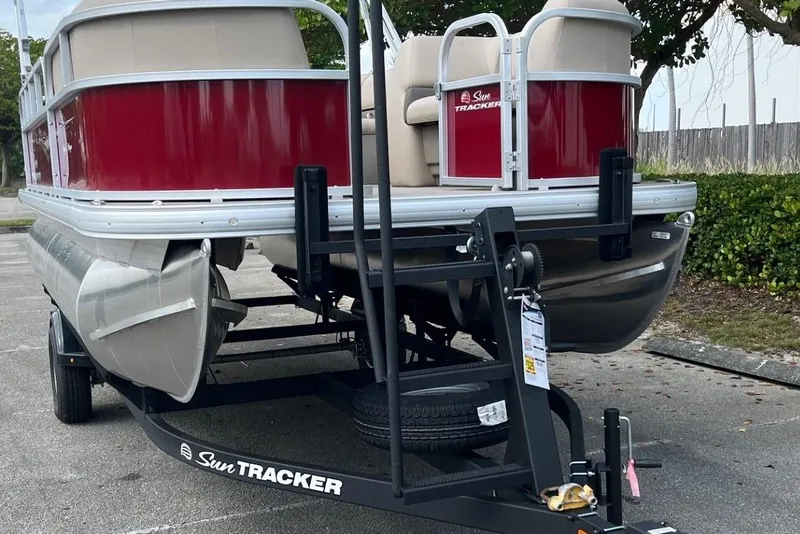 Slide: The Image of 2025 Sun Tracker Party Barge 18 DLX pontoon boat on trailer, parked outdoors. - 2