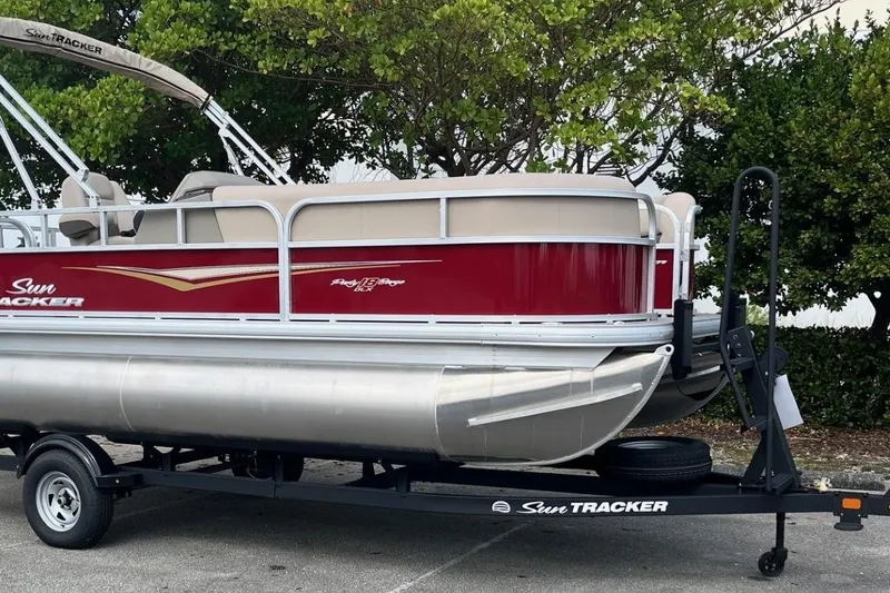 Slide: The Image of 2025 Sun Tracker Party Barge 18 DLX pontoon boat on trailer, parked outdoors. - 3