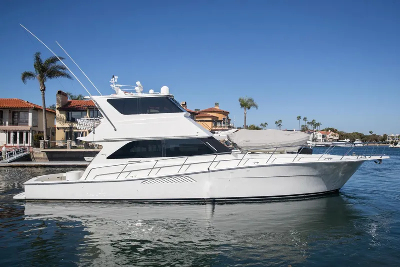 Slide: The Image of 1999 Viking 58 Enclosed Bridge yacht docked near waterfront homes, under clear blue sky. - 46