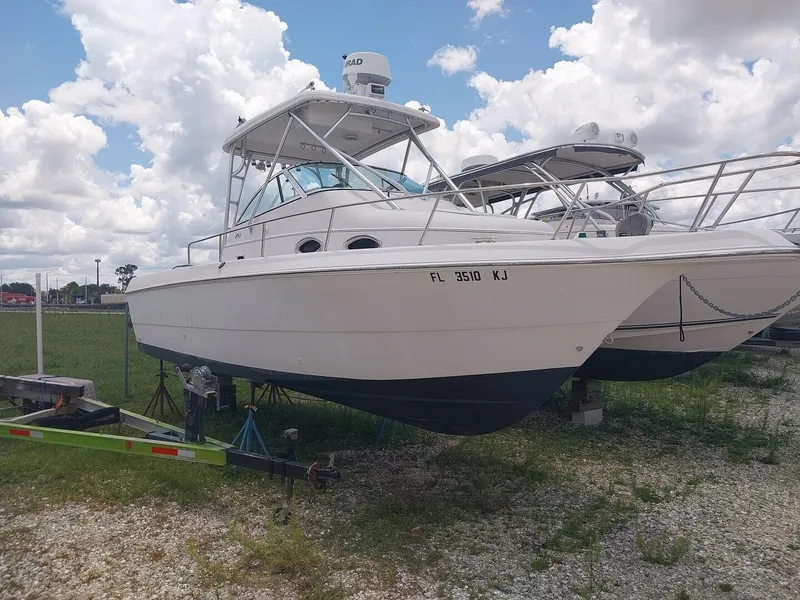 The Image of 1997 Pro-Line 251 Walkaround boat on trailer, parked on gravel with cloudy sky background. - 1