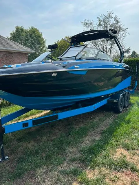 The Image of 2022 Centurion Fi23 boat on trailer, black and blue design, parked outdoors. - 1