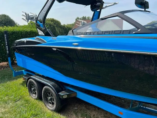 Slide: The Image of 2022 Centurion Fi23 boat in vibrant blue, parked on grass, showcasing sleek design and dual-axle trailer. - 2