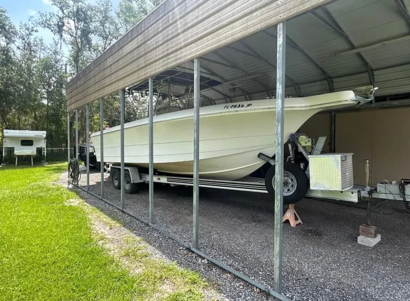 Slide: The Image of 1996 Pro-Line 27 CC boat on trailer under metal shelter, surrounded by greenery. - 11