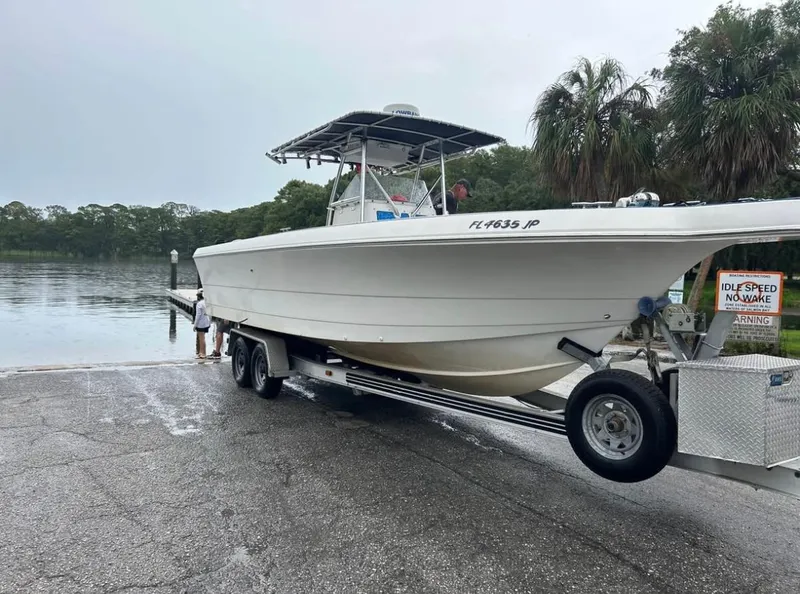 Slide: The Image of 1996 Pro-Line 27 CC boat on trailer near water, surrounded by trees and overcast sky. - 6