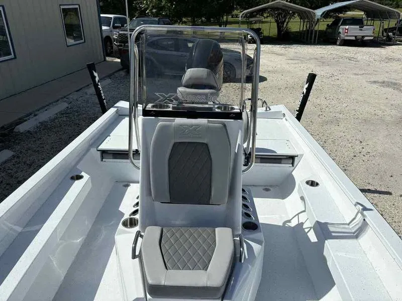 Slide: The Image of 2026 Xpress H22B boat interior with gray seating and console, parked outdoors. - 14