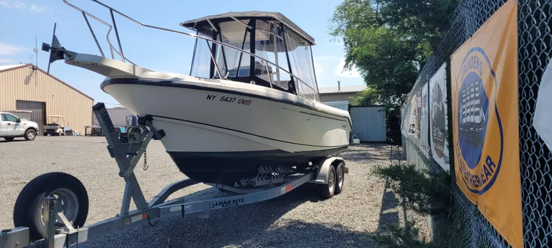 The Image of Boston Whaler 240 Outrage 2000 on trailer, parked outdoors near a fence with banners. - 0