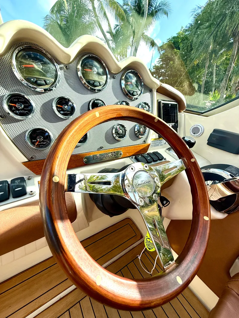 Slide: The Image of 2015 Chris-Craft Launch 32 dashboard with wooden steering wheel and gauges, surrounded by palm trees. - 43