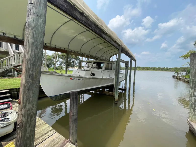 The Image of 1995 Stuart Angler 33 Downeast boat docked under a canopy on a calm lake. - 0