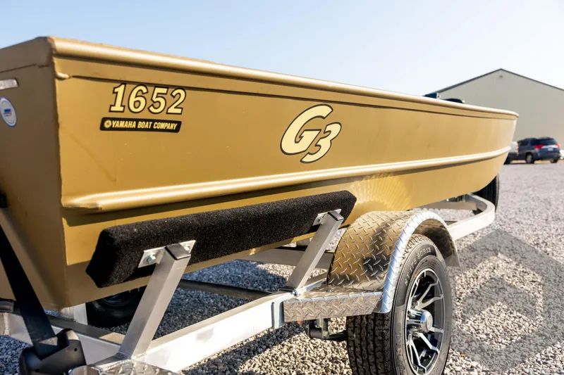 Slide: The Image of 2025 G3 Gator Tough 1652 VBW boat on a trailer, parked on gravel. - 15