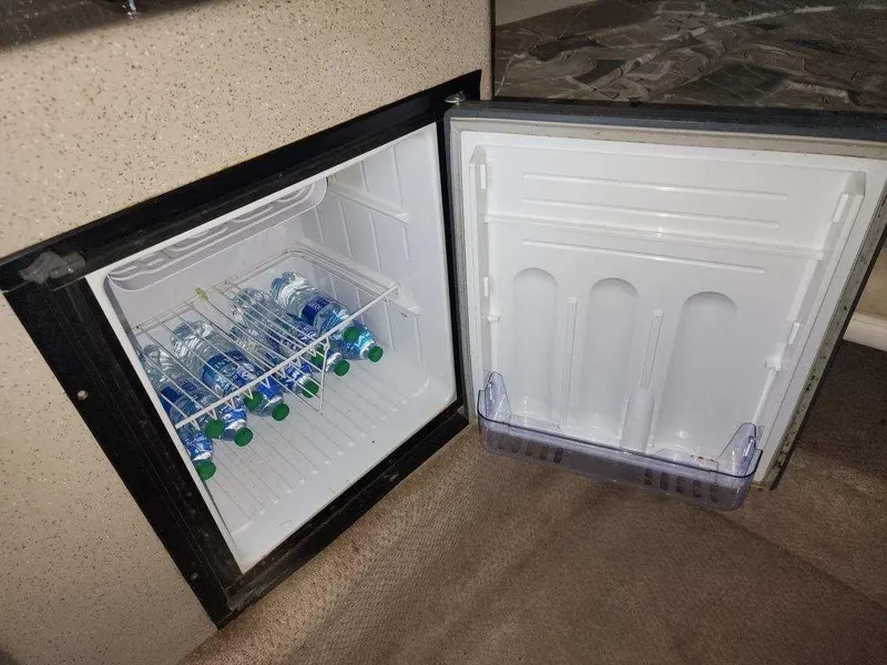 Slide: The Image of Mini fridge stocked with water bottles inside a 2000 Rinker 270 Express Cruiser. - 13