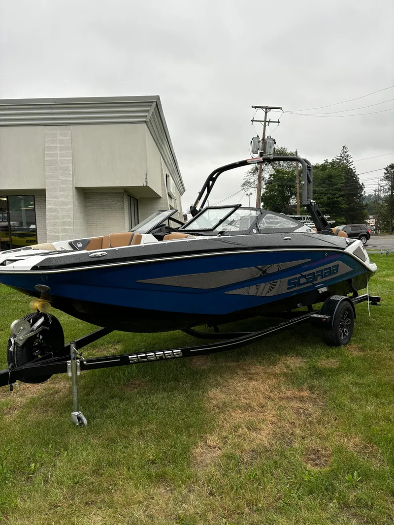 The Image of 2024 Scarab 215 H.O. Platinum boat on trailer, parked on grass near a building. - 1