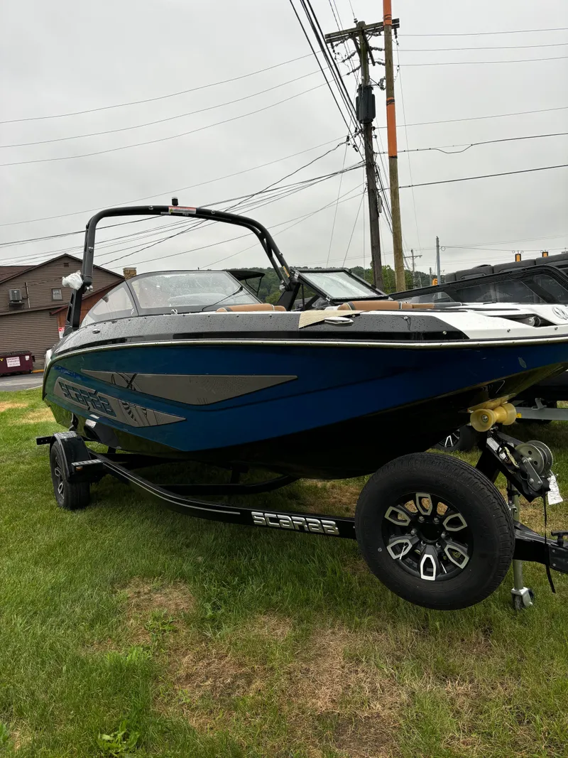 Slide: The Image of 2024 Scarab 215 H.O. Platinum boat on trailer, parked on grass. - 2