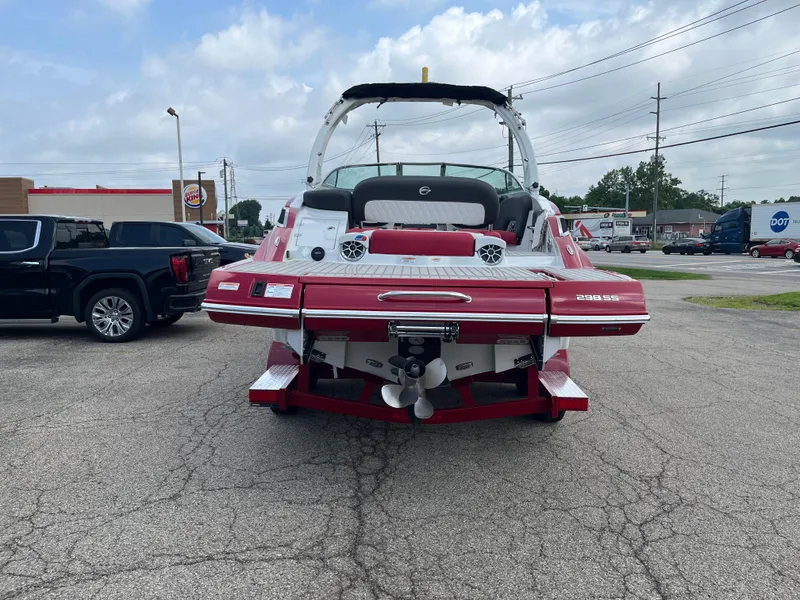 Slide: The Image of 2026 Crownline 298 SS boat, red and white, parked in a lot with vehicles nearby. - 2
