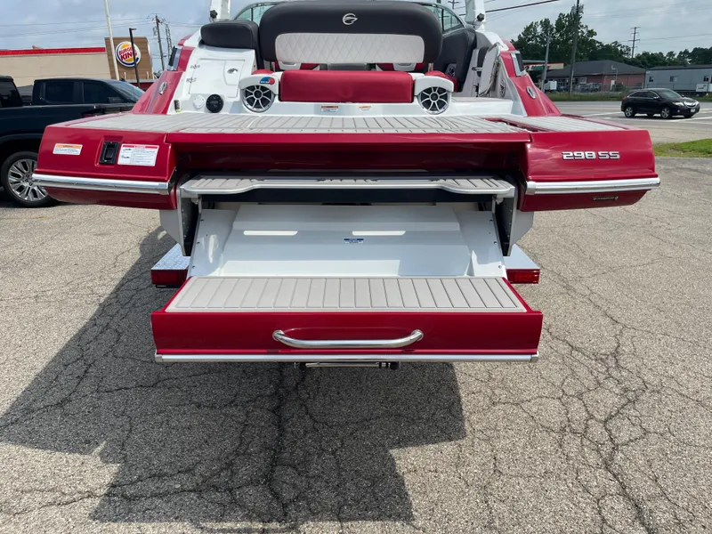 Slide: The Image of 2026 Crownline 298 SS boat with open rear storage compartment, parked on pavement. - 22