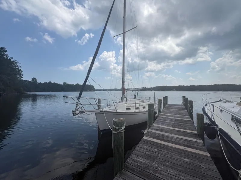 The Image of 1986 Island Packet IP27 Cutter sailboat docked by a wooden pier under a cloudy sky. - 0
