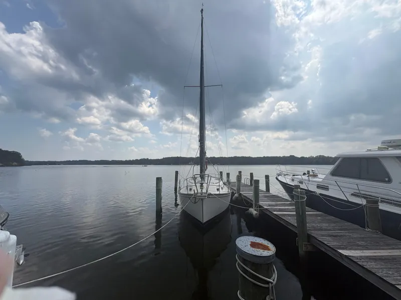 Slide: The Image of 1986 Island Packet IP27 Cutter docked at a serene marina under cloudy skies. - 2