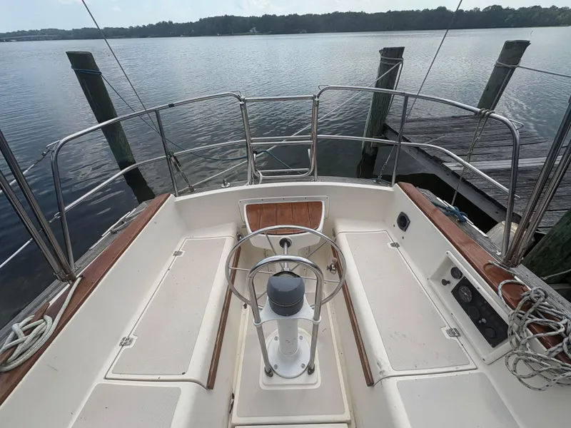 Slide: The Image of 1986 Island Packet IP27 Cutter sailboat cockpit with steering wheel, docked by calm waters. - 7