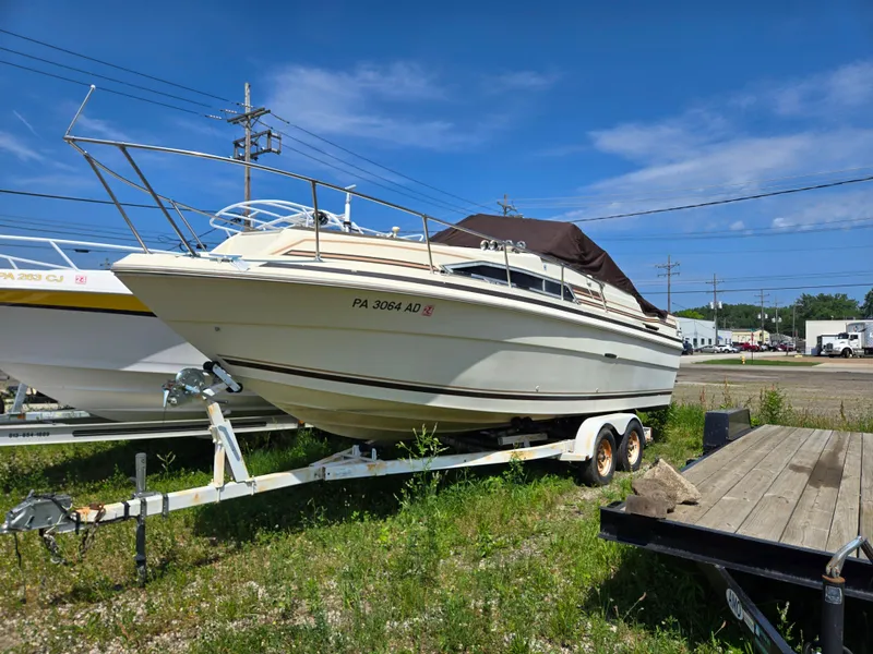 The Image of 1983 Sea Ray Weekender boat on trailer, parked outdoors under clear blue sky. - 1
