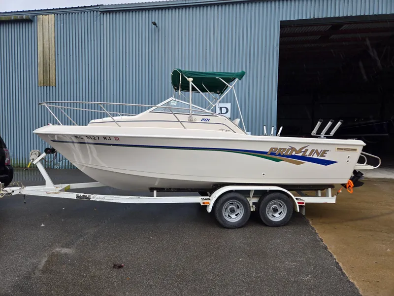 Slide: The Image of 1997 Pro-Line 201 Walkaround boat on trailer, parked outside a blue warehouse. - 0