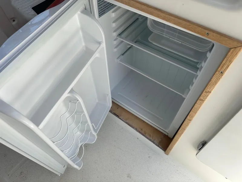 Slide: The Image of Open fridge inside 1992 Bayliner 2359 Trophy boat, showing empty shelves and door storage. - 27
