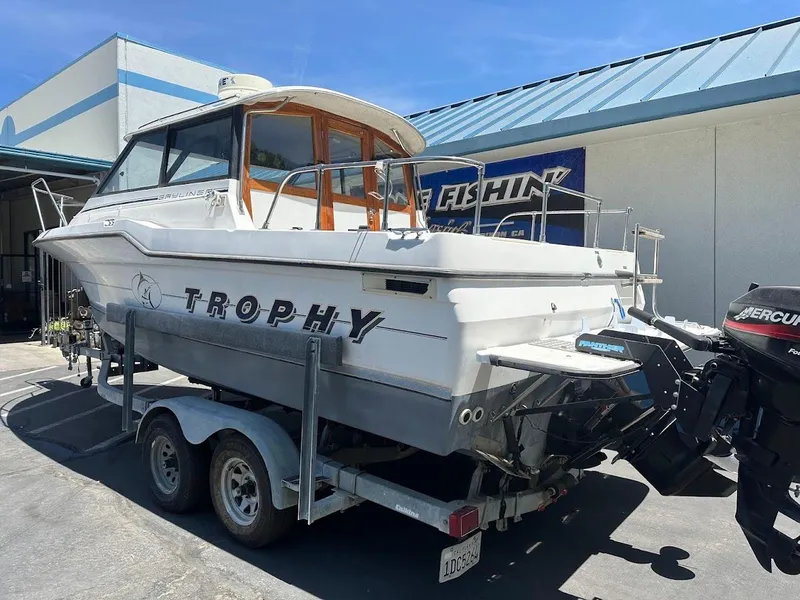 Slide: The Image of 1992 Bayliner 2359 Trophy boat on trailer, parked outside a building under clear blue sky. - 8